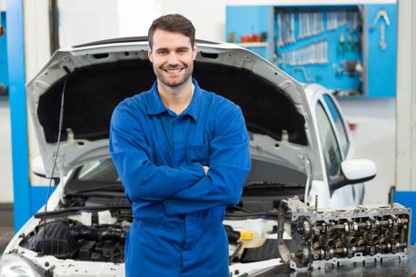 mechanic guy smiling with a car behind