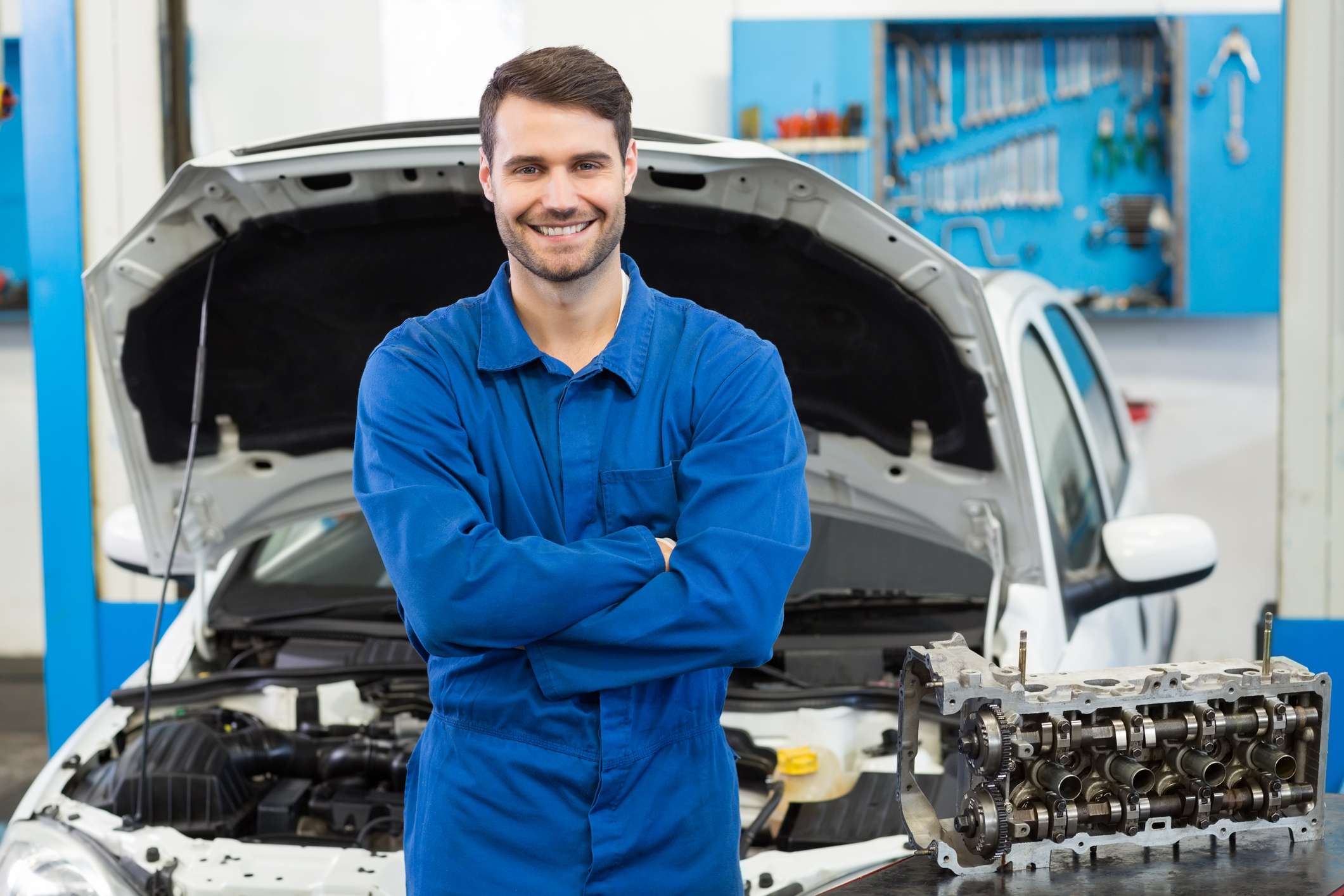 mechanic guy smiling with a car behind